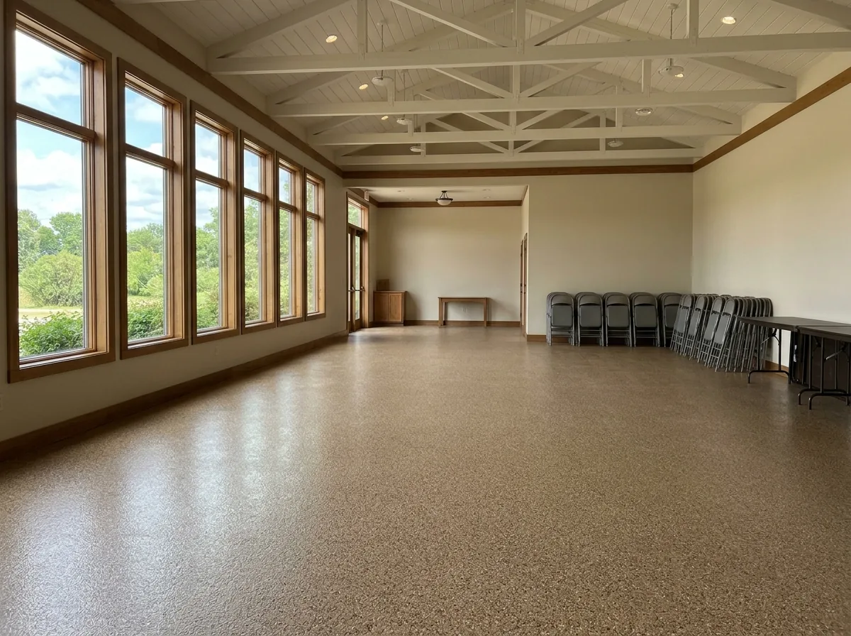 Large church fellowship hall with a tan and brown flake epoxy floor, folding tables stacked against the wall and tall windows