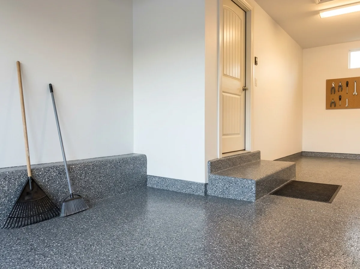 Garage stem wall, the low concrete curb at the base of the drywall, coated in the same gray flake as the floor, with the coating running up and over a concrete step into the house